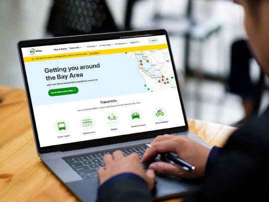 Picture of a person sitting at a laptop showing the new site homepage on the screen