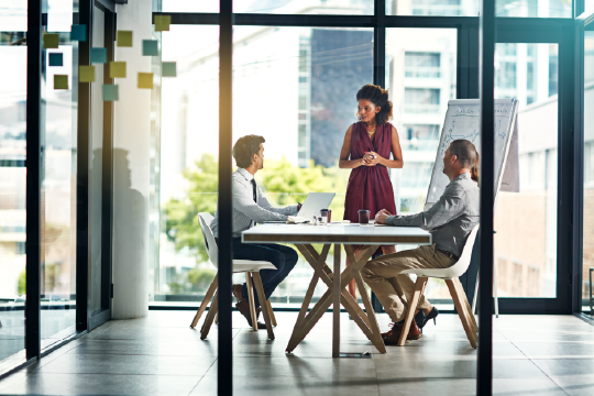 Woman presenting in a small conference room to her colleagues.