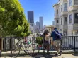 Two people next to a bicycle peer down over a railing at a bustling cityscape below