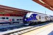 A sleek blue train pulling into a train station next to a red and white train