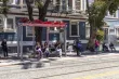 People waiting under a red awning on a bench at a bus stop
