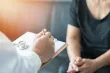 A doctor writing on a clipboard as a patient sits nearby