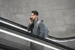 A man speaking into his phone mic while riding an escalator