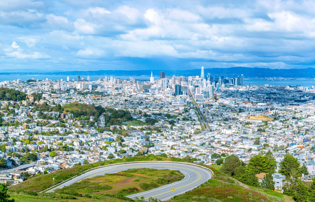 Overhead view of cityscape with a blue sky in the background and a winding road in the foreground